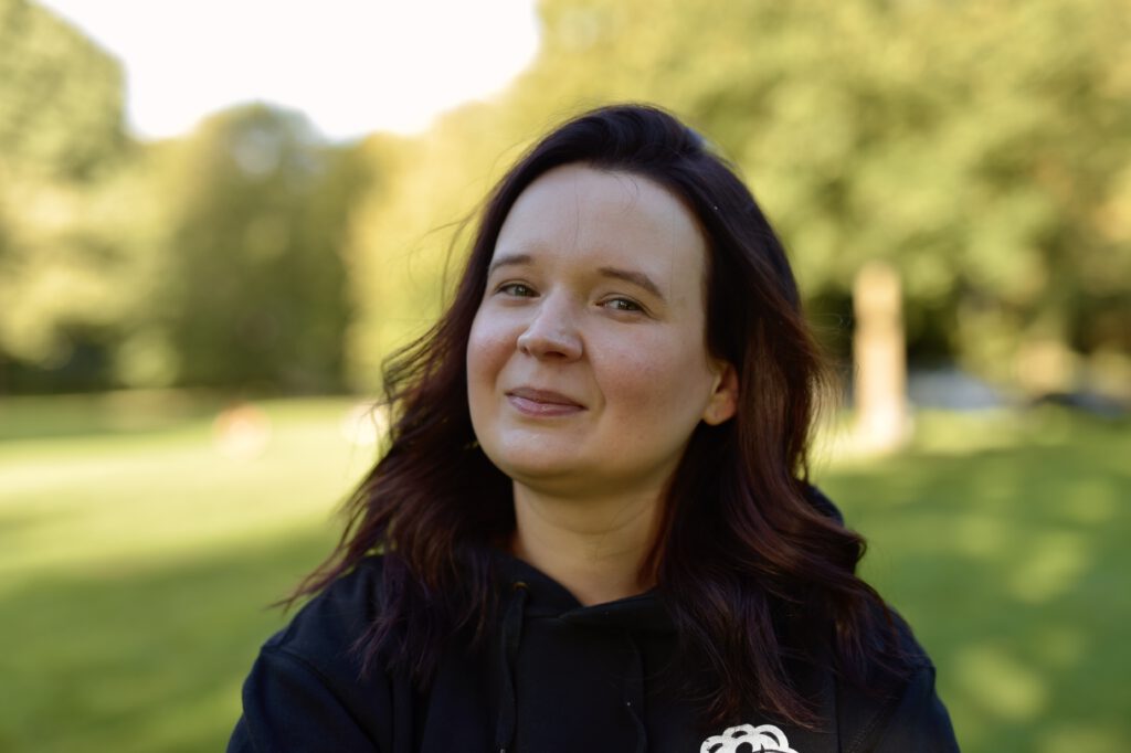 Jessica Hennig im Freien vor grünen Bäumen.